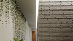 Ein Korridor mit einer Backsteinwand rechts und einer Wand mit einem grünen, blättrigen Muster links. In der Mitte steht ein Blumentopf.