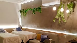 Ein modernes Hotelzimmer mit zwei Betten, einer Couch, einem kleinen Tisch und einer hängenden Pflanze.