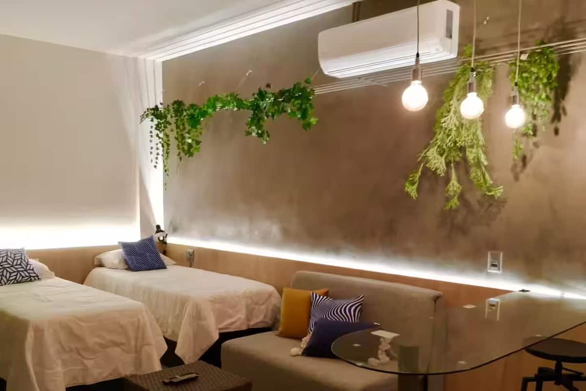 Una habitación de hotel moderna con dos camas, un sofá, una mesita y una planta colgante.