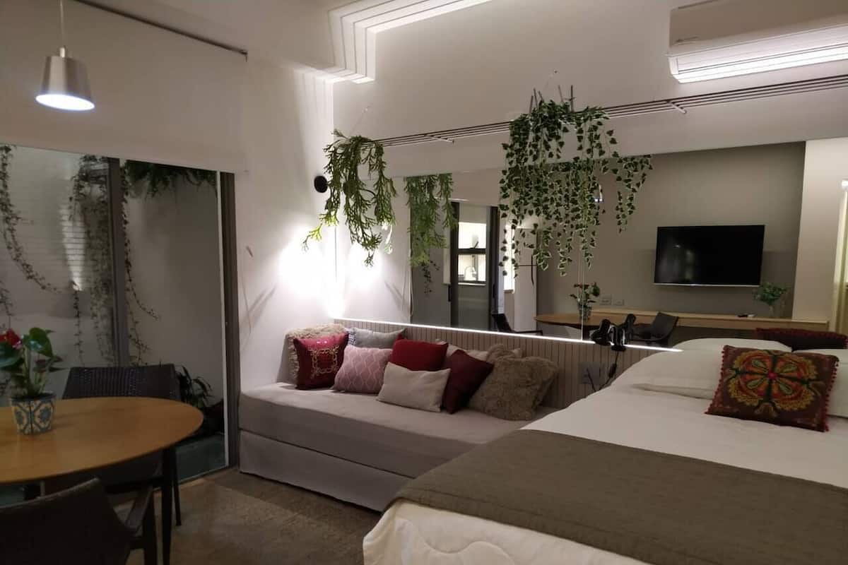 Una habitación de hotel moderna con sofá, cama, mesa de comedor y plantas colgantes.