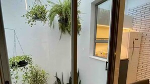 Ein modernes Interieur mit einer Glastür, die zu einem kleinen Außenbereich mit Holzterrasse und Pflanzkübeln führt.
