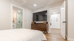 Ein Schlafzimmer mit einem großen Bett, einem Schminktisch, einem Fernseher und einem begehbaren Kleiderschrank.