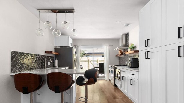 Eine moderne Küche mit weißen Schränken, einer Holz Arbeitsplatte und zwei Barhocker.