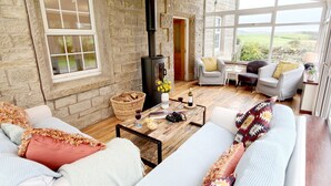 A cozy living room with stone walls, a fireplace, and a view of the countryside. - Bush Nook House (Brampton)