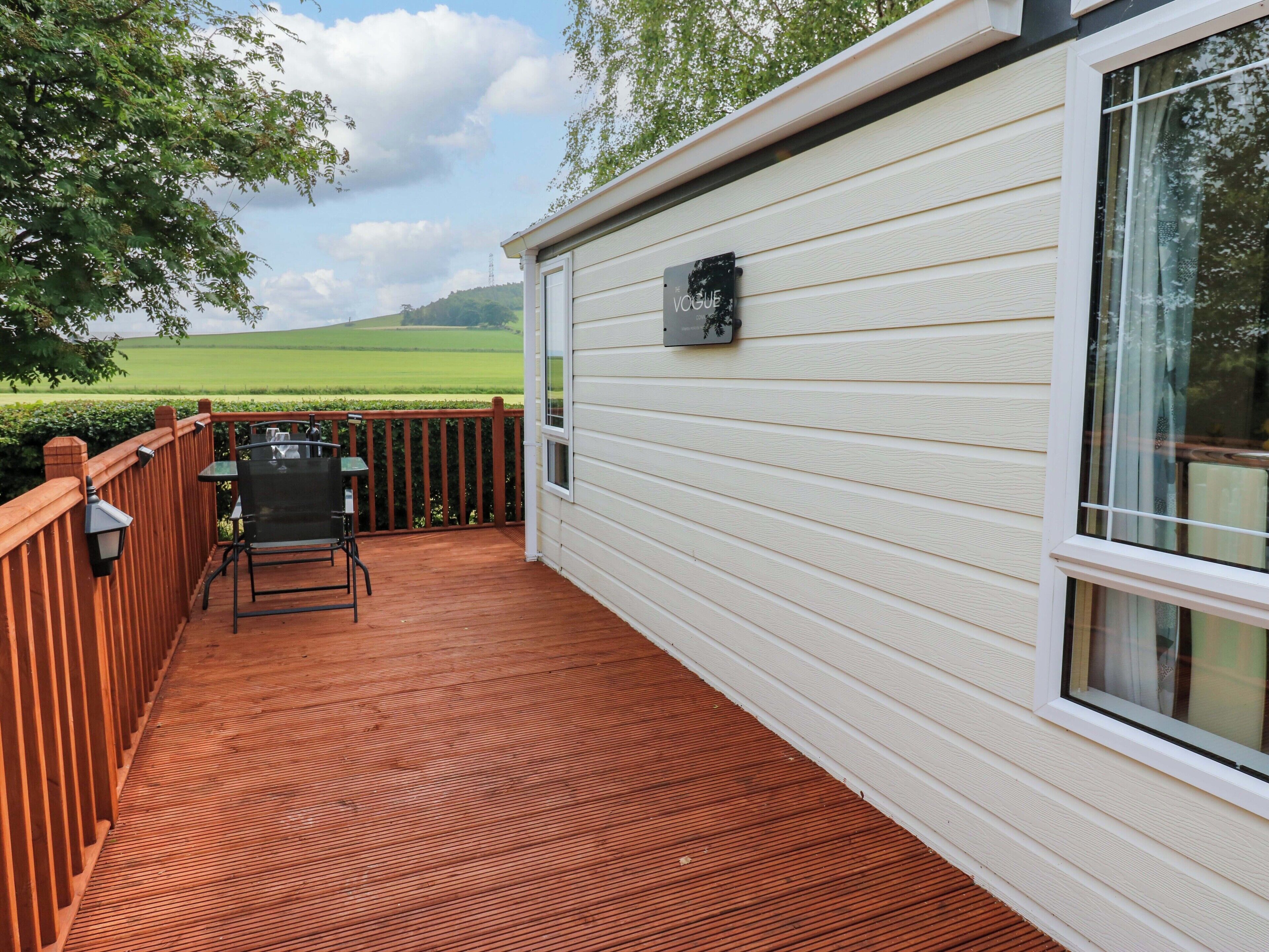 A covered patio with a wooden deck, a table and chairs, and a view of a green field.