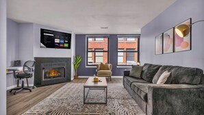 A modern living room with a fireplace, a mounted TV, and a large window. - Charming loft in lovely DT Cleveland - Free parking - Balcony - Gym (Cleveland)