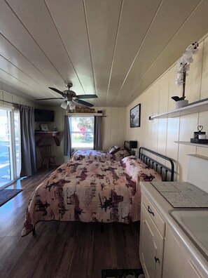 A bedroom with a bed, a ceiling fan, a desk, a chair, and a window with curtains.