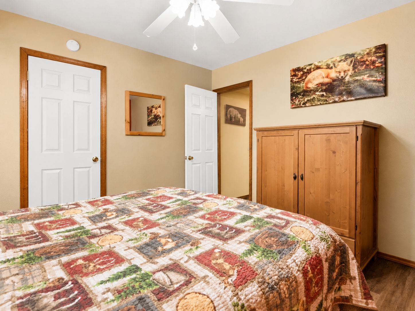 Quarto com cama, duas portas, espelho, quadro e guarda-roupa de madeira.