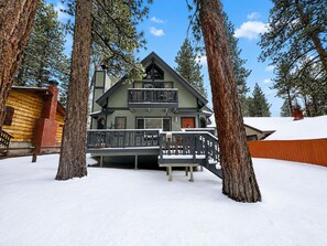 A multi-story log cabin with a balcony, surrounded by tall pine trees and covered in snow. - Sunset Chalet (Big Bear Lake)