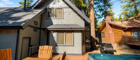 A two-story cabin with a deck, outdoor seating, and a hot tub.