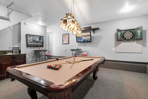Une table de billard avec des billes et des queues de billard, un jeu de fléchettes et un téléviseur fixé au mur.