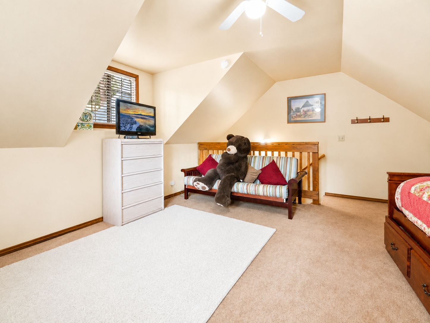A bedroom with a sloped ceiling, a bed, a sofa, a dresser, and a television.
