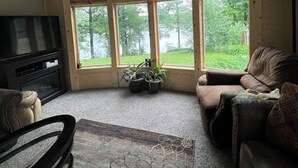A cozy living room with a fireplace, a large window with a view of greenery, and a mounted television. - Apple River Retreat home in Amery  (Amery)