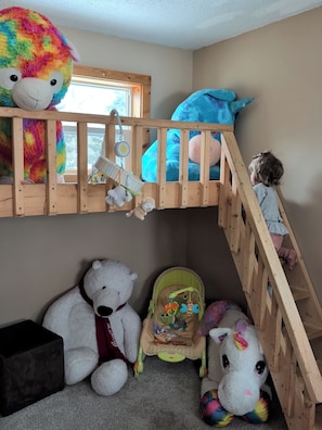 Una cama litera infantil con ventana, un osito de peluche, un peluche de unicornio y un cochecito.