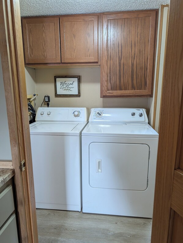 A laundry room with two white front-loading washers and dryers, wooden cabinets above, and a sign on the wall.