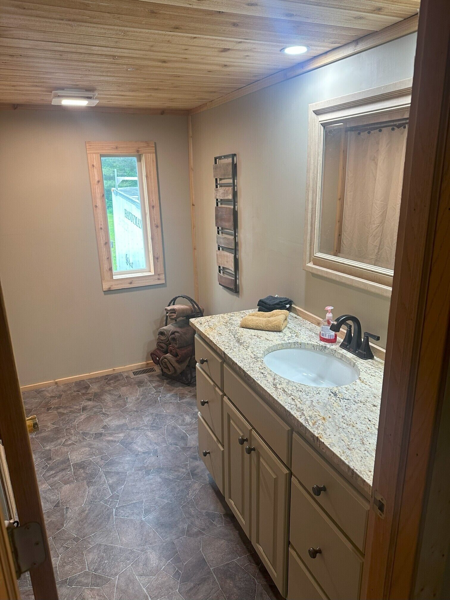 A bathroom with a granite countertop sink, wooden cabinets, a towel rack, and a window with a view of a building.