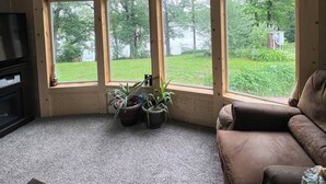 A room with a sloped ceiling, wooden walls, a large window, a brown leather couch, and two potted plants. - Apple River Retreat home in Amery  (Amery)