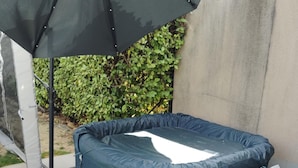 A hot tub with a cover, a water heater, and a white container on a patio.