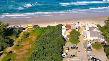 An aerial view of a coastal area with a beach, parking lot, and buildings.