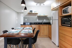 A modern kitchen with wooden cabinets, a black countertop, and a dining table set for four. - Studio Shopping OKA Floripa - SOK226 (Florianopolis)
