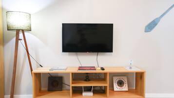 A modern living room with a flat-screen TV mounted on the wall, a wooden entertainment unit with a lamp, a book, and a remote control.
