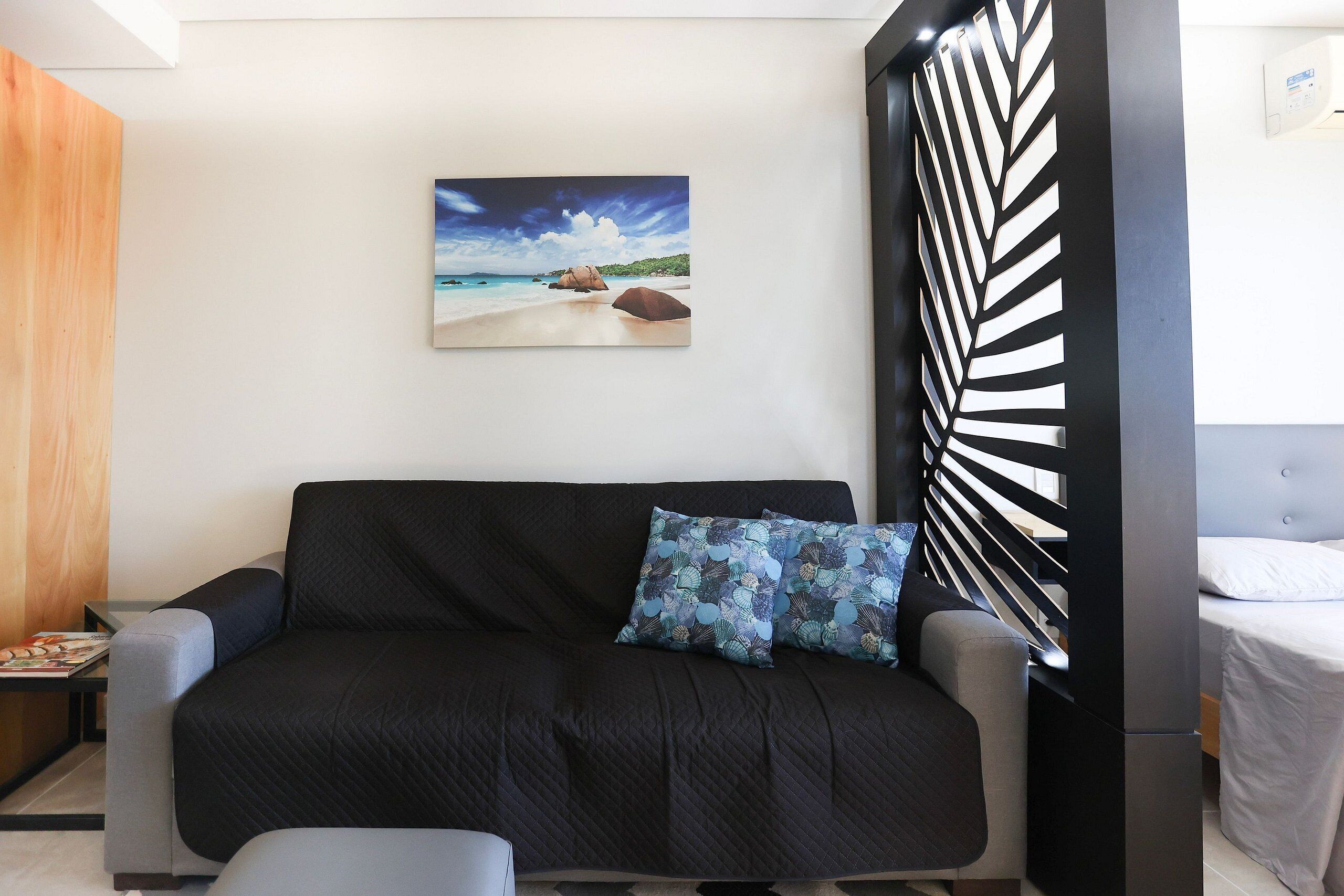 Una sala de estar moderna con un sofá negro, un panel decorativo y una pintura de una escena playera.