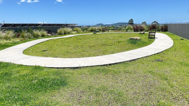 Un espacio al aire libre con jardines, un sendero curvo, bancos y vistas a colinas distantes.