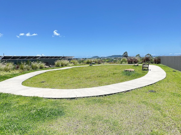 Un espacio al aire libre con jardines, un sendero curvo, bancos y vistas a colinas distantes.