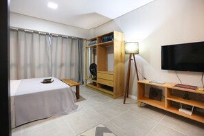 A bedroom with a bed, a wooden wardrobe, a TV, and a small table. - Studio Shopping OKA Floripa - SOK226 (Florianopolis)