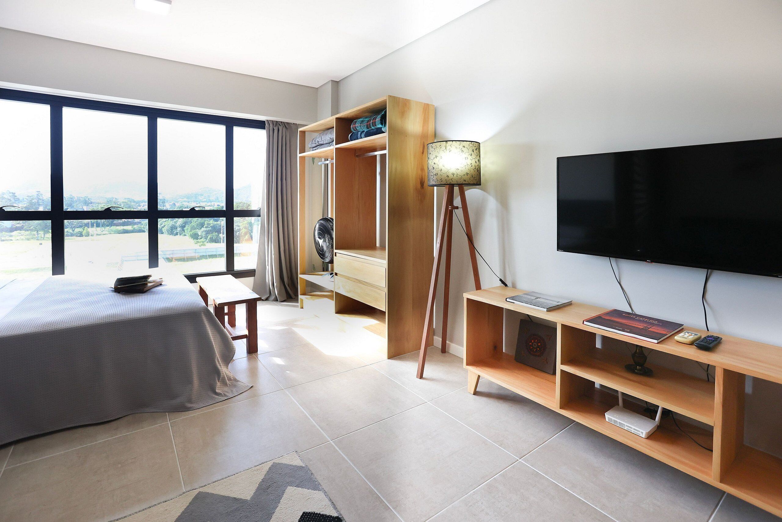 Ein Hotelzimmer mit einem Bett, einem Fernseher, einer Holzablage und einem großen Fenster.
