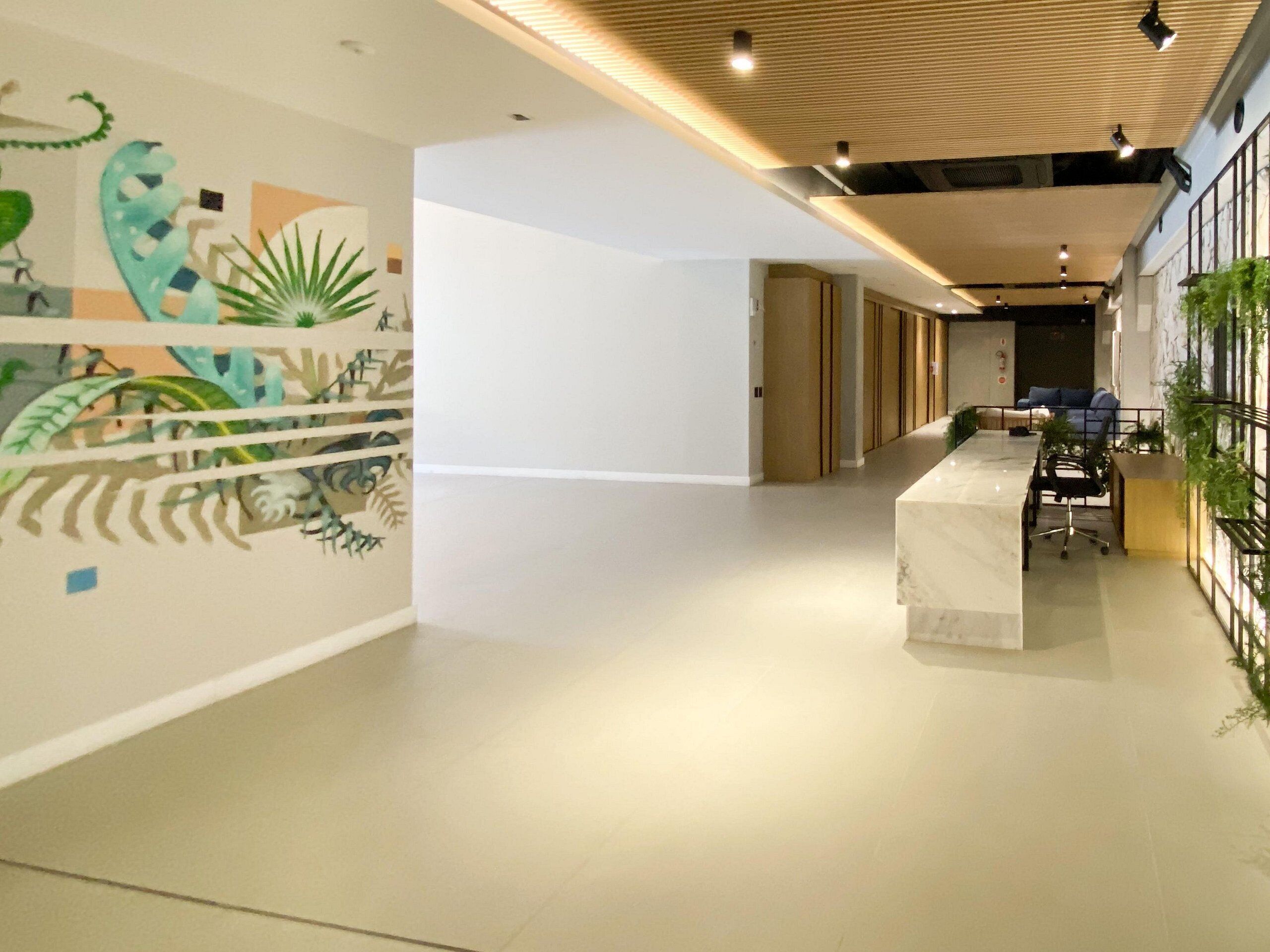 A modern office space with a long reception desk, a mural with abstract designs, and a plant wall.