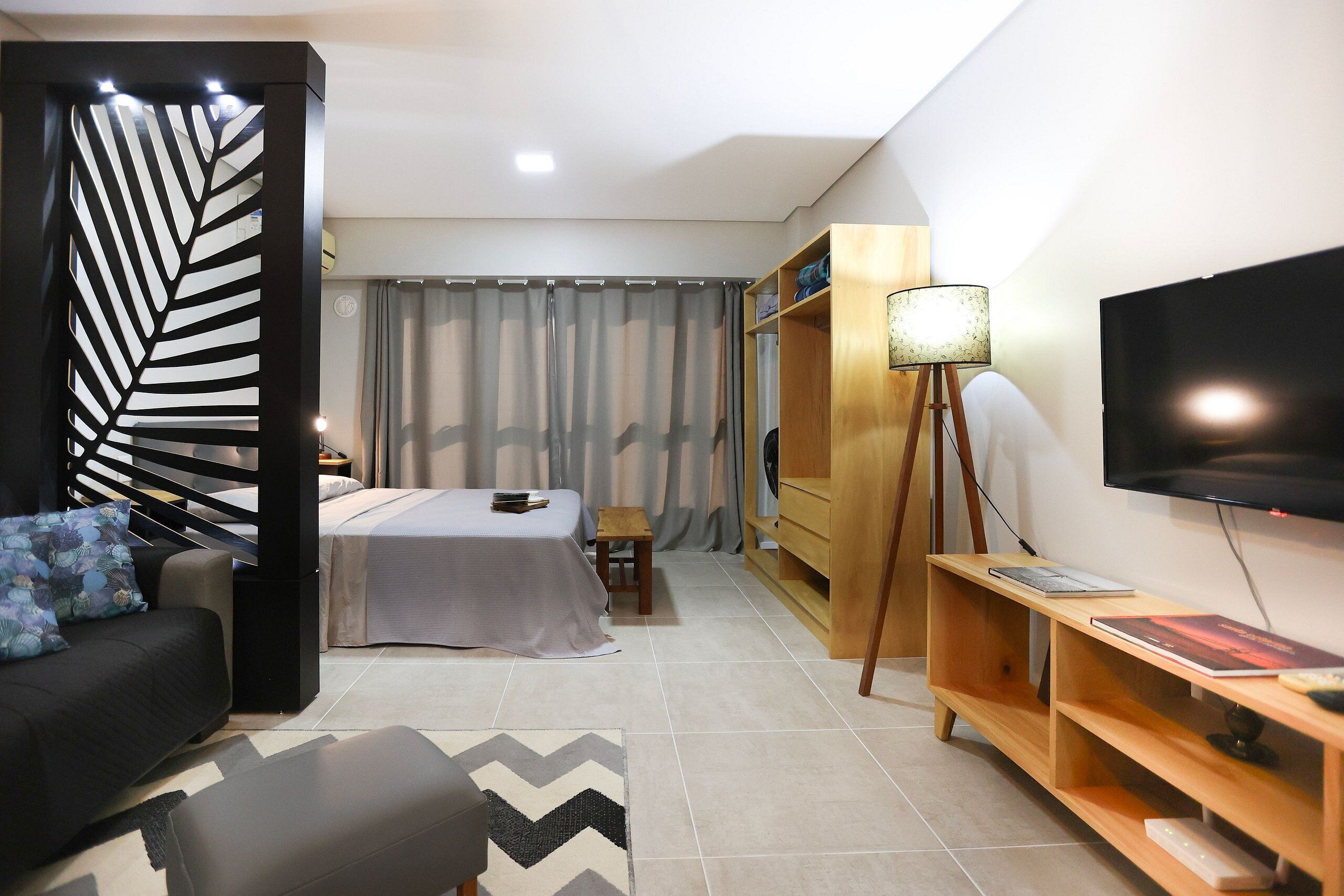 A modern hotel room with a bed, a sofa, a TV, and a wooden entertainment unit.