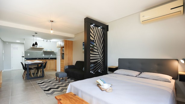 A modern hotel room with a bed, bedside table, and a view of the kitchen.