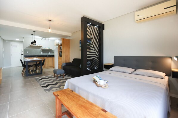 A modern hotel room with a bed, bedside table, and a view of the kitchen.