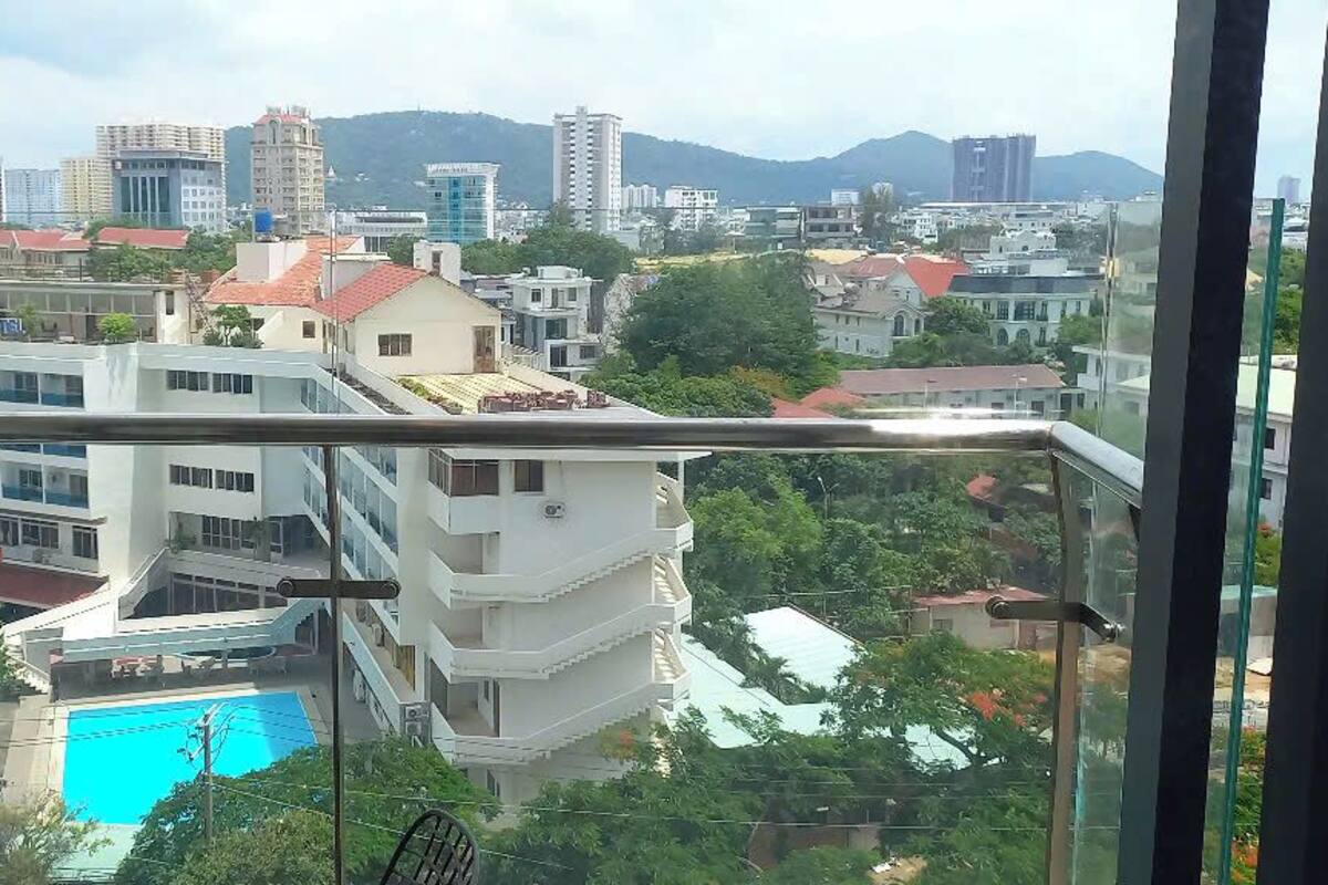 A view from a balcony overlooking a swimming pool, with buildings and greenery in the background.