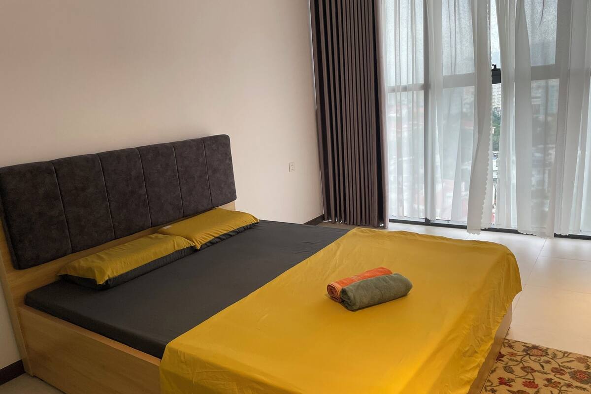 A bed with a dark headboard, a yellow bedspread, and a rolled towel on the footboard.