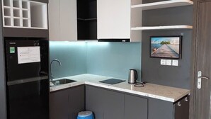 A compact kitchen with a refrigerator, sink, and a kettle. There is a small trash bin and a picture on the wall. - Beachside Condo CSJ TOWER - Nice View (Ho Chi Minh City)