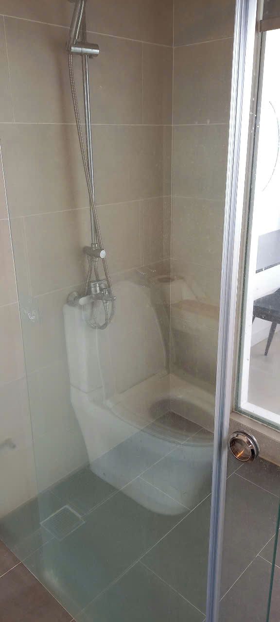 A glass-enclosed shower stall with a handheld showerhead and a wall-mounted faucet.