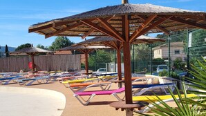 A beachside area with sun loungers, a thatched umbrella, and a fenced enclosure.