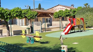A playground with a slide and swings, surrounded by a fence and trees.