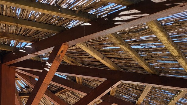 A pool area with a wooden pergola overhead and a view of a mountain in the background.