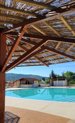 Zona de piscina con una pérgola de madera y vistas a una montaña al fondo.
