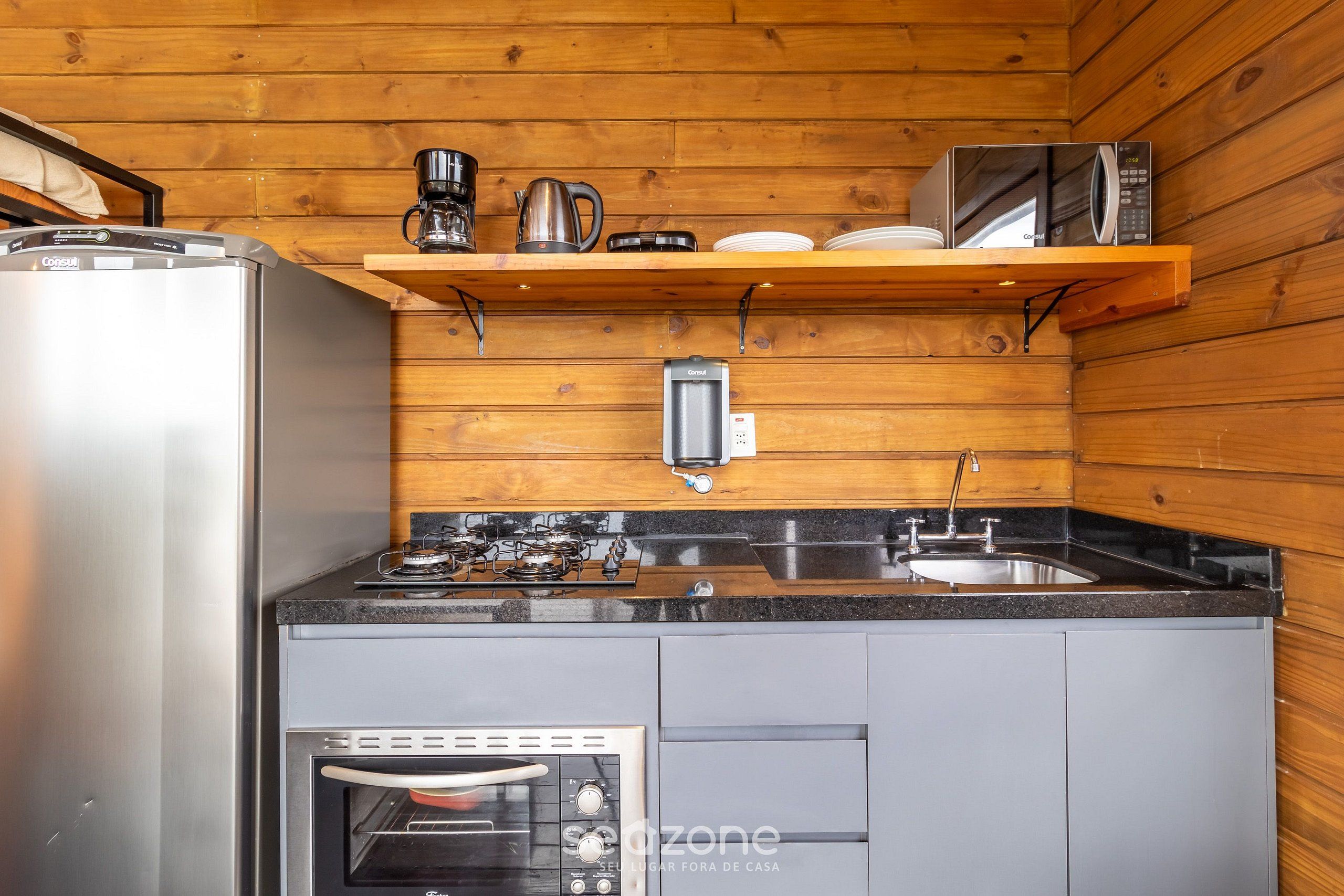 Una cucina compatta con frigorifero, fornello, forno e macchina del caffè su un ripiano.