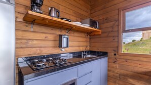 Een kleine keuken met een gasfornuis, een koffiezetapparaat en een waterkoker op een houten plank.