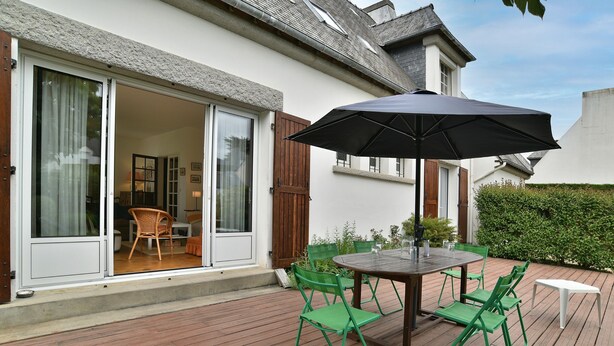 A patio with a table and chairs, a sliding glass door, and a wooden deck.