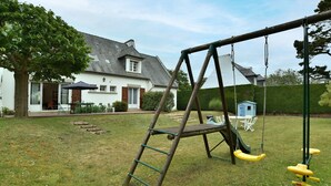 A backyard with a swing set, a ladder, and a small playhouse.