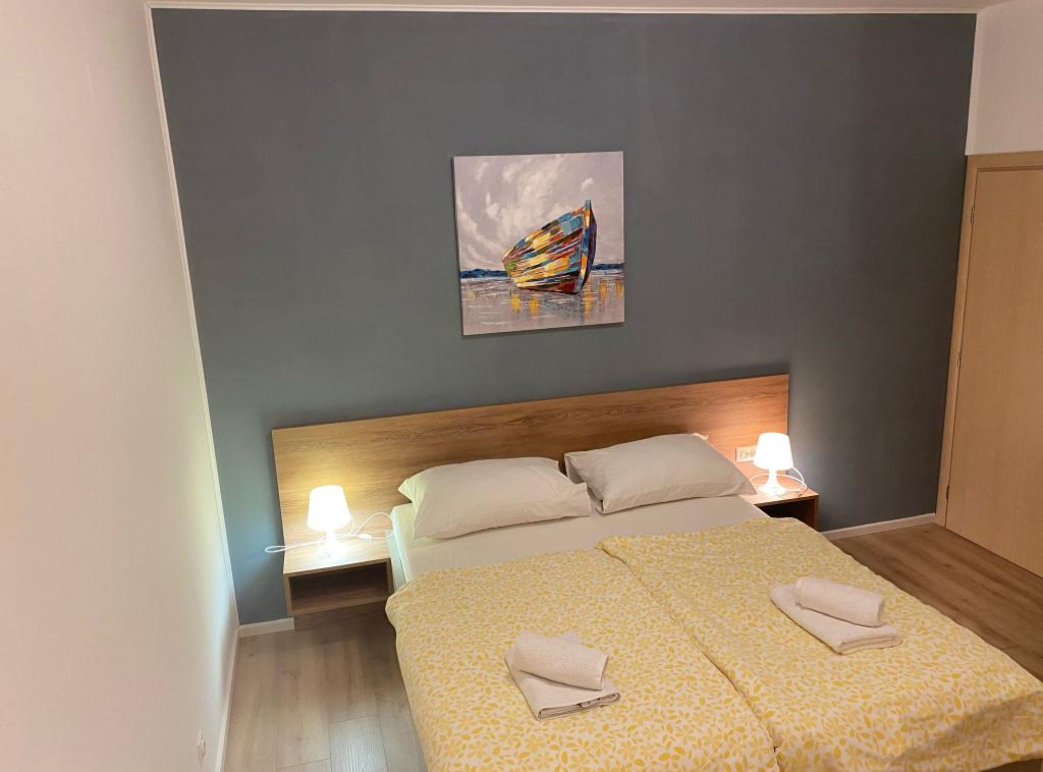 A hotel room with a bed, two bedside tables, a night lamp, and a painting on the wall.