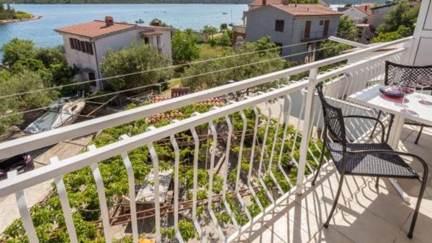 Ein Balkon mit Tisch und Stühlen, mit Blick auf einen See mit Booten und Häusern.