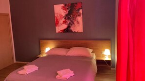 Ein Hotelzimmer mit einem Bett, zwei Nachttischlampen, einem Wandbild im abstrakten Stil und einem roten Vorhang.