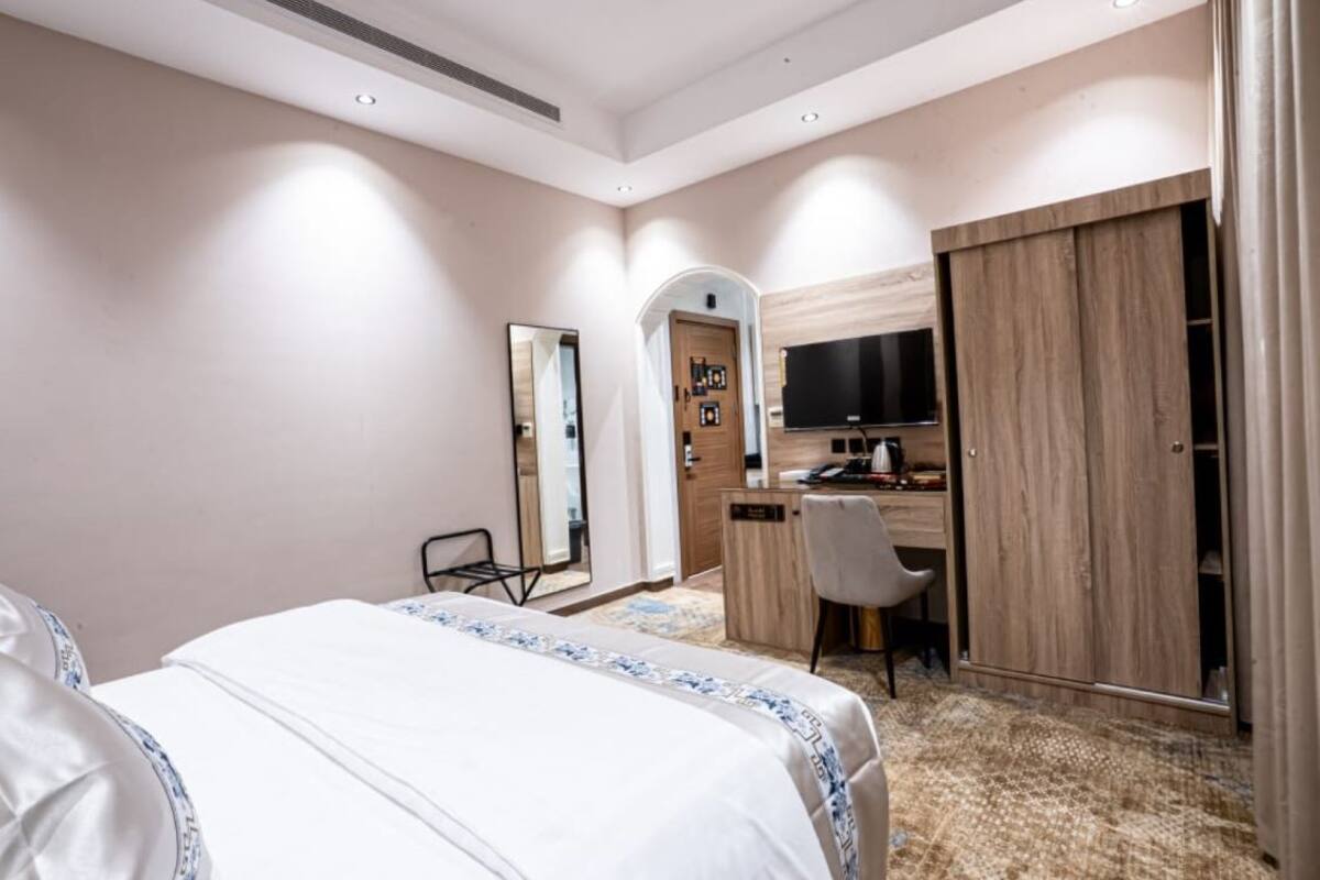 A hotel room with a bed, a desk, a chair, a TV, and a wardrobe.